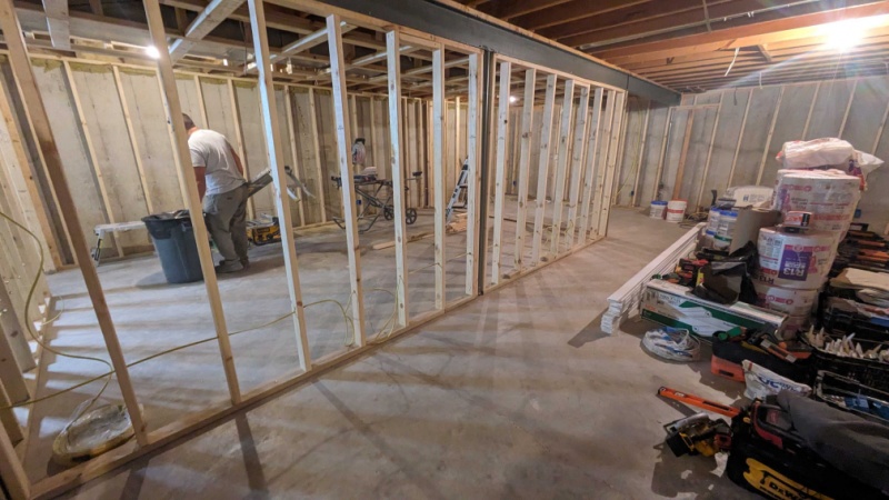 Interior of a home basement under construction with exposed wooden framing, construction tools, and materials scattered around.